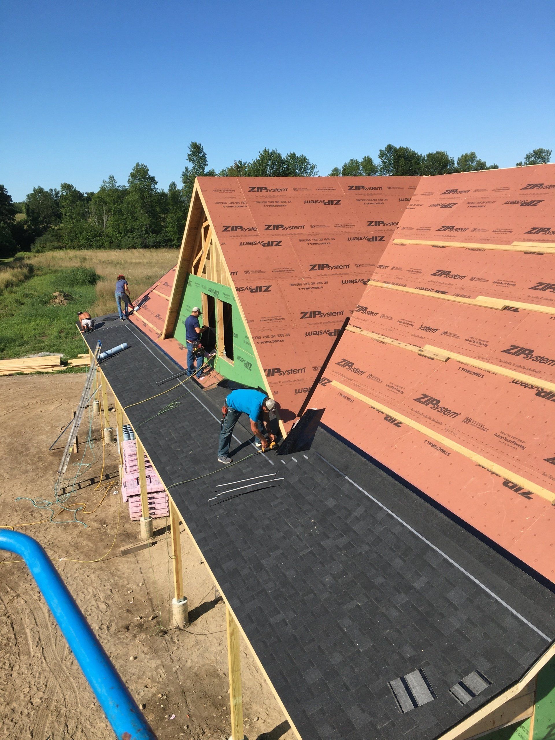 Workers roofing a house, laying black underlayment on a steep A-frame roof.