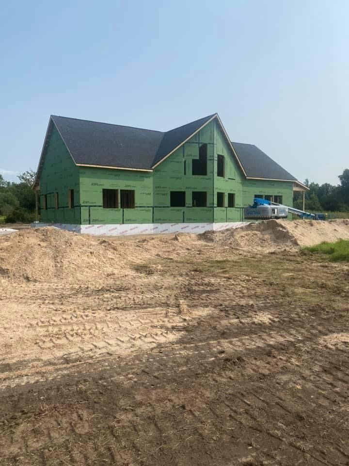 Green house under construction on a bare dirt lot beneath a clear sky