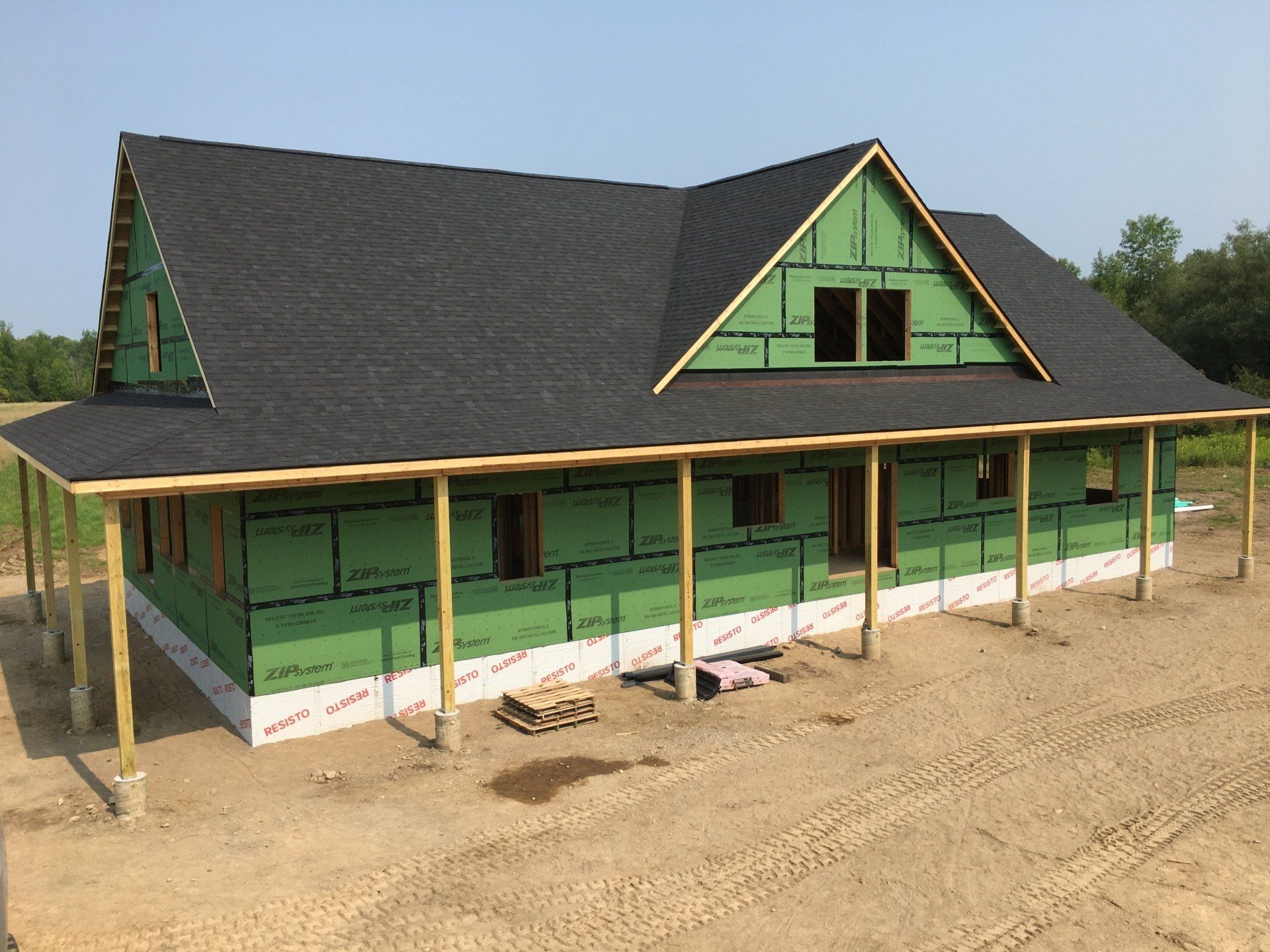 Partially built green house with black roof and covered porch on a dirt lot