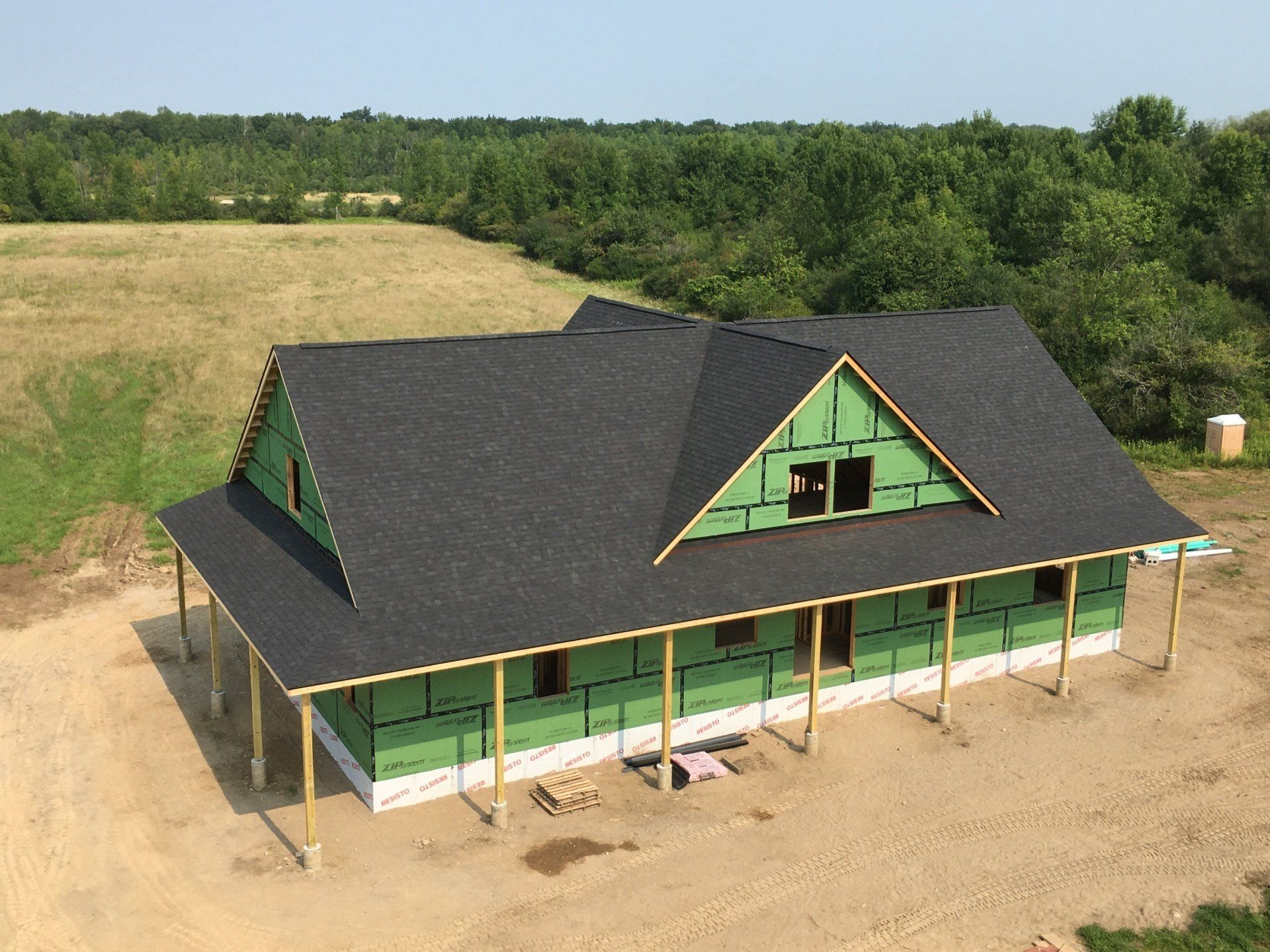 Partially built green house with black roof on a dirt lot surrounded by trees