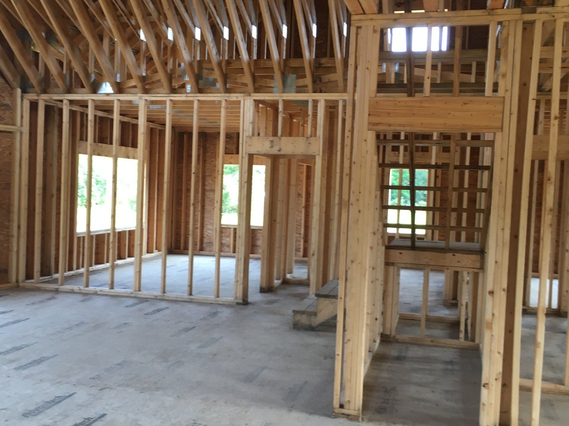 Interior of a house under construction with exposed wooden framing and concrete floor.