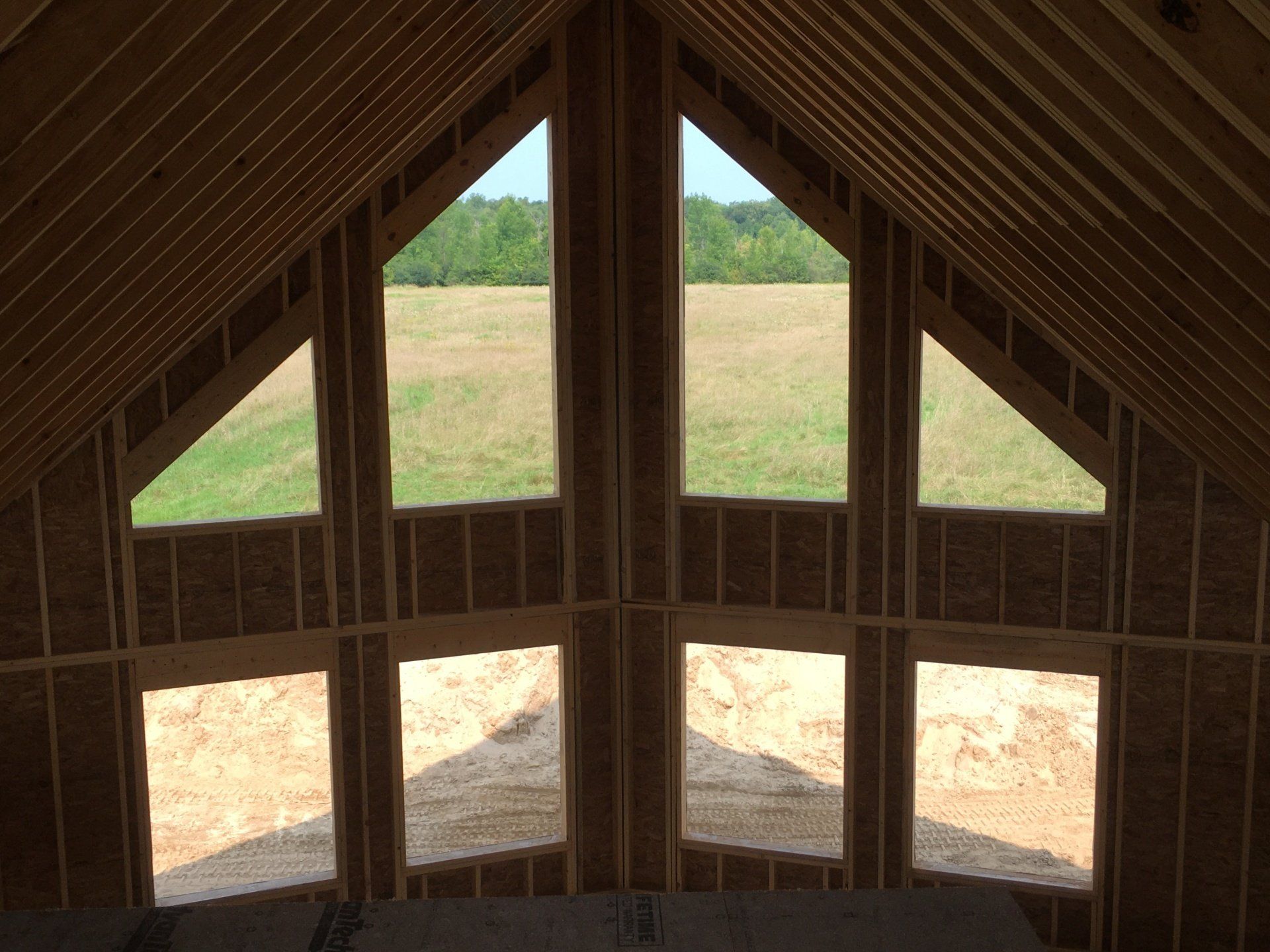 Wooden attic interior with peaked rafters and three small windows overlooking a field