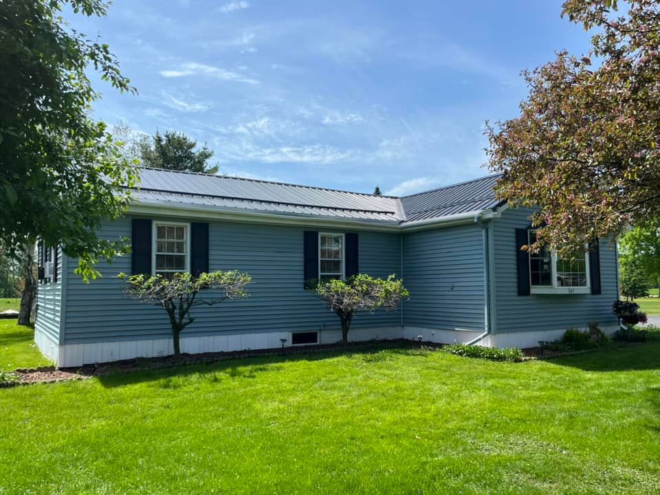 A blue house with black shutters is sitting on top of a lush green lawn.