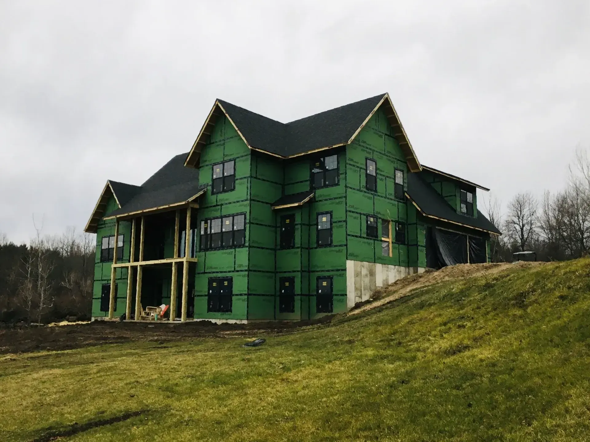 Green house under construction on a grassy hillside, with dark roof and exposed framing.