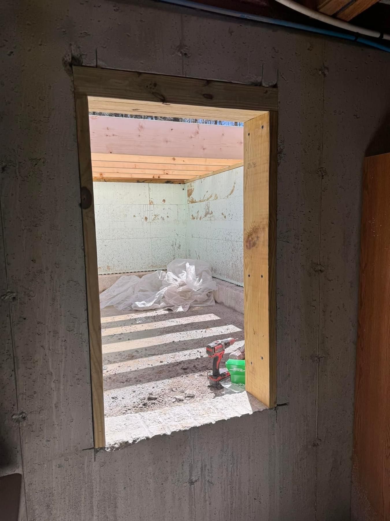 Unfinished room with a narrow window opening to a sunlit, debris-strewn courtyard.