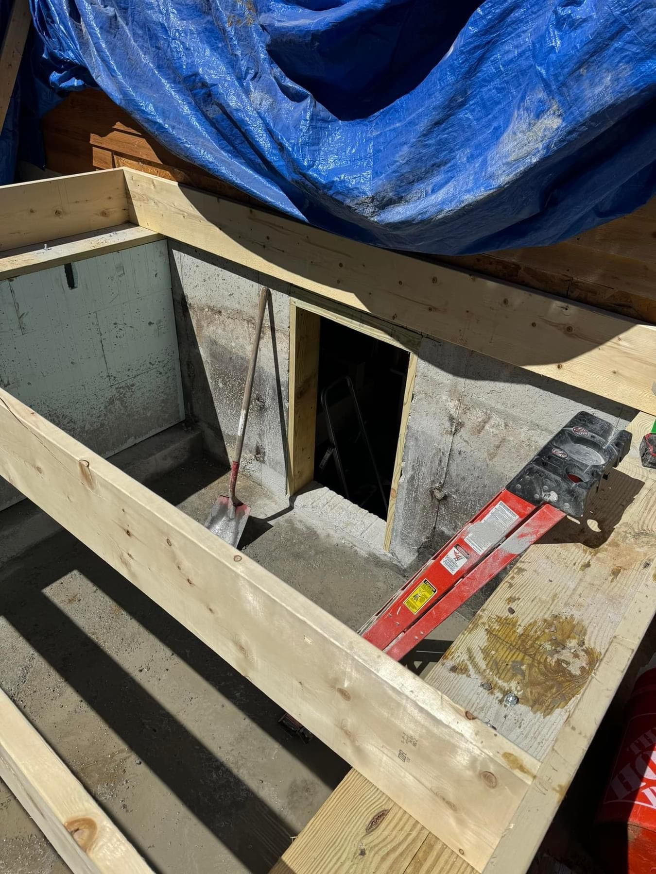 Partially built wooden floor framing around a square opening, with a level and blue tarp on top