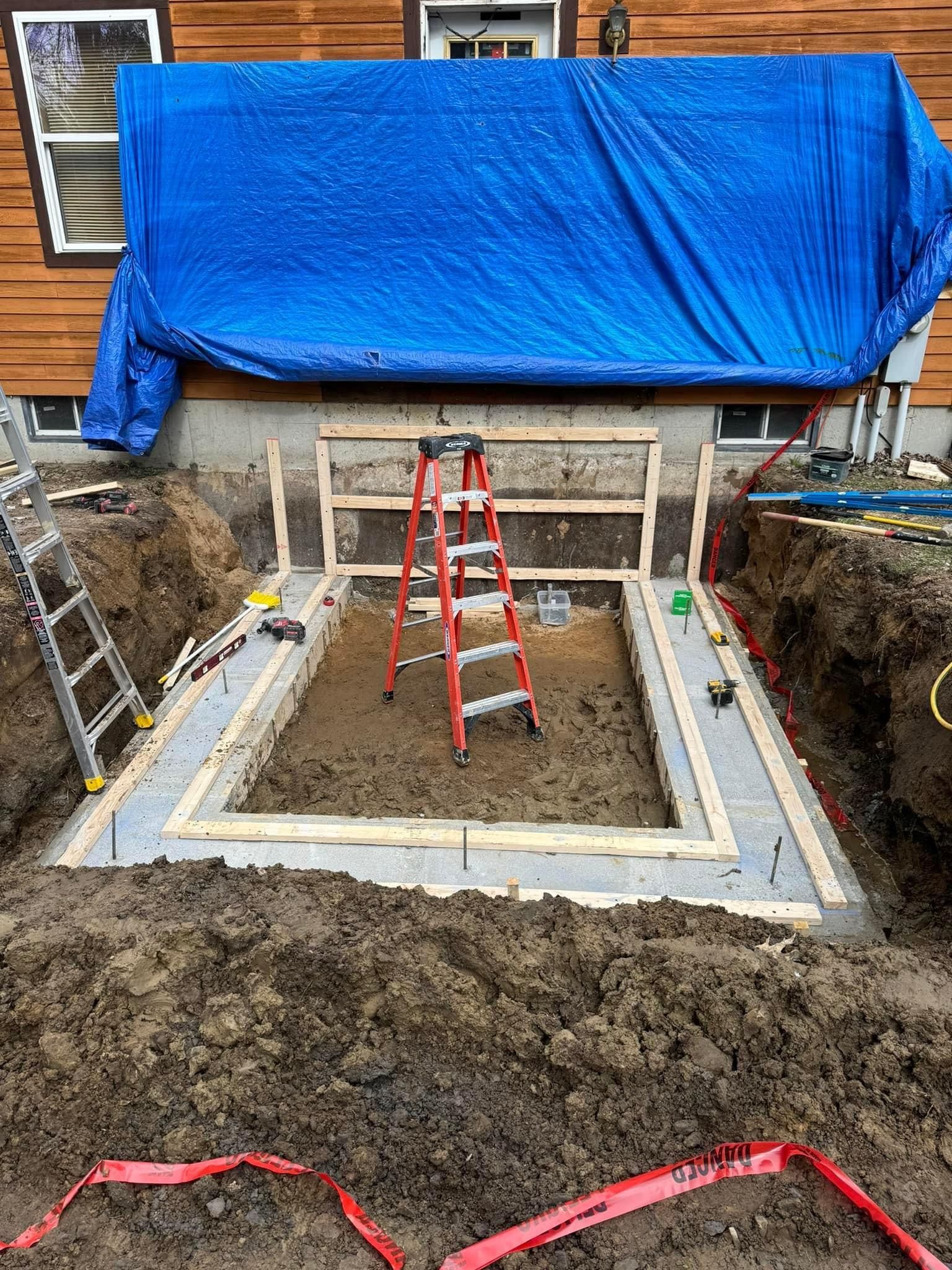 Backyard excavation with concrete foundation, red ladder, and blue tarp covering the house above.