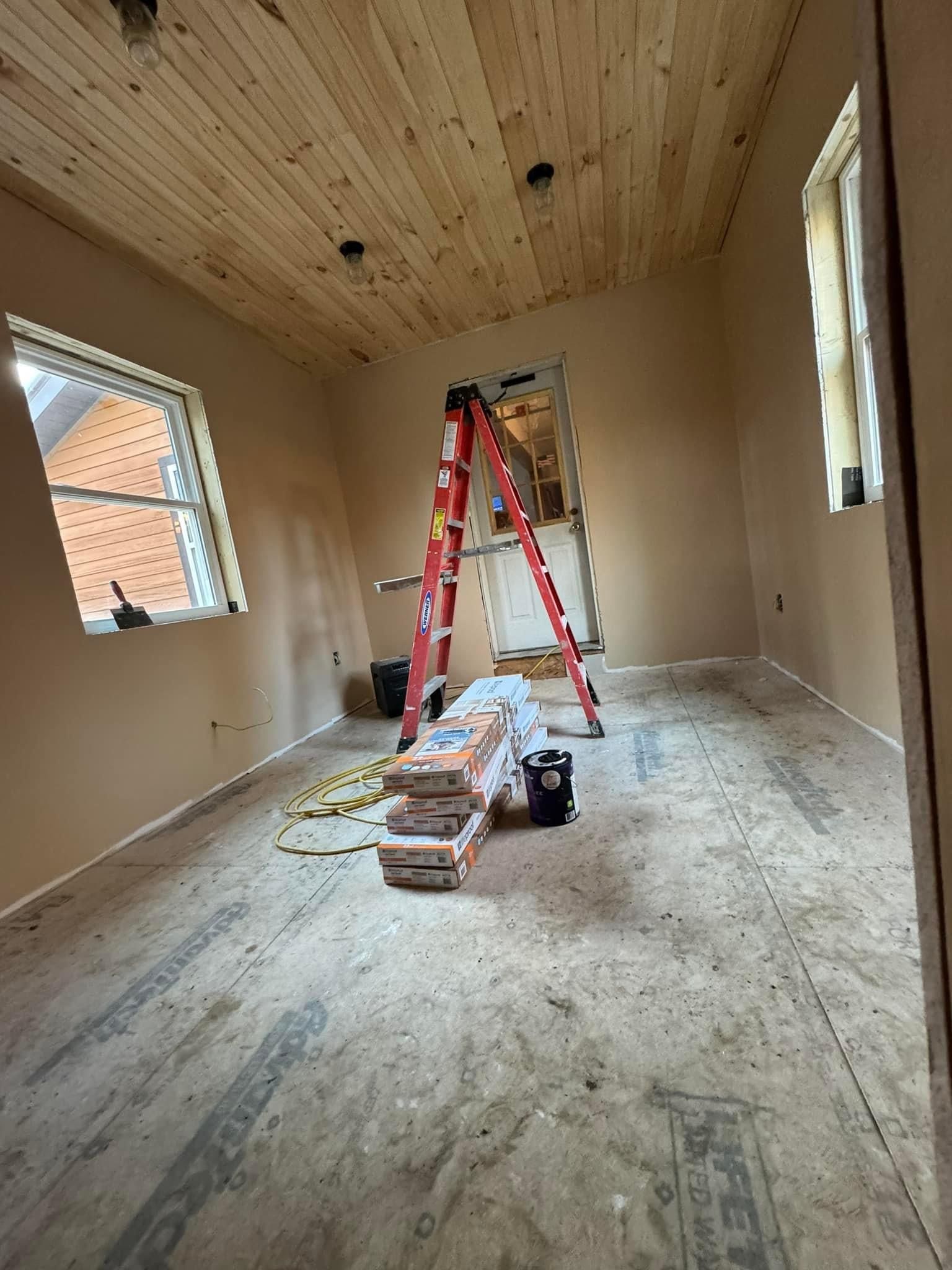 Partially finished room with wood plank ceiling, ladders, tools, and construction materials on the floor.