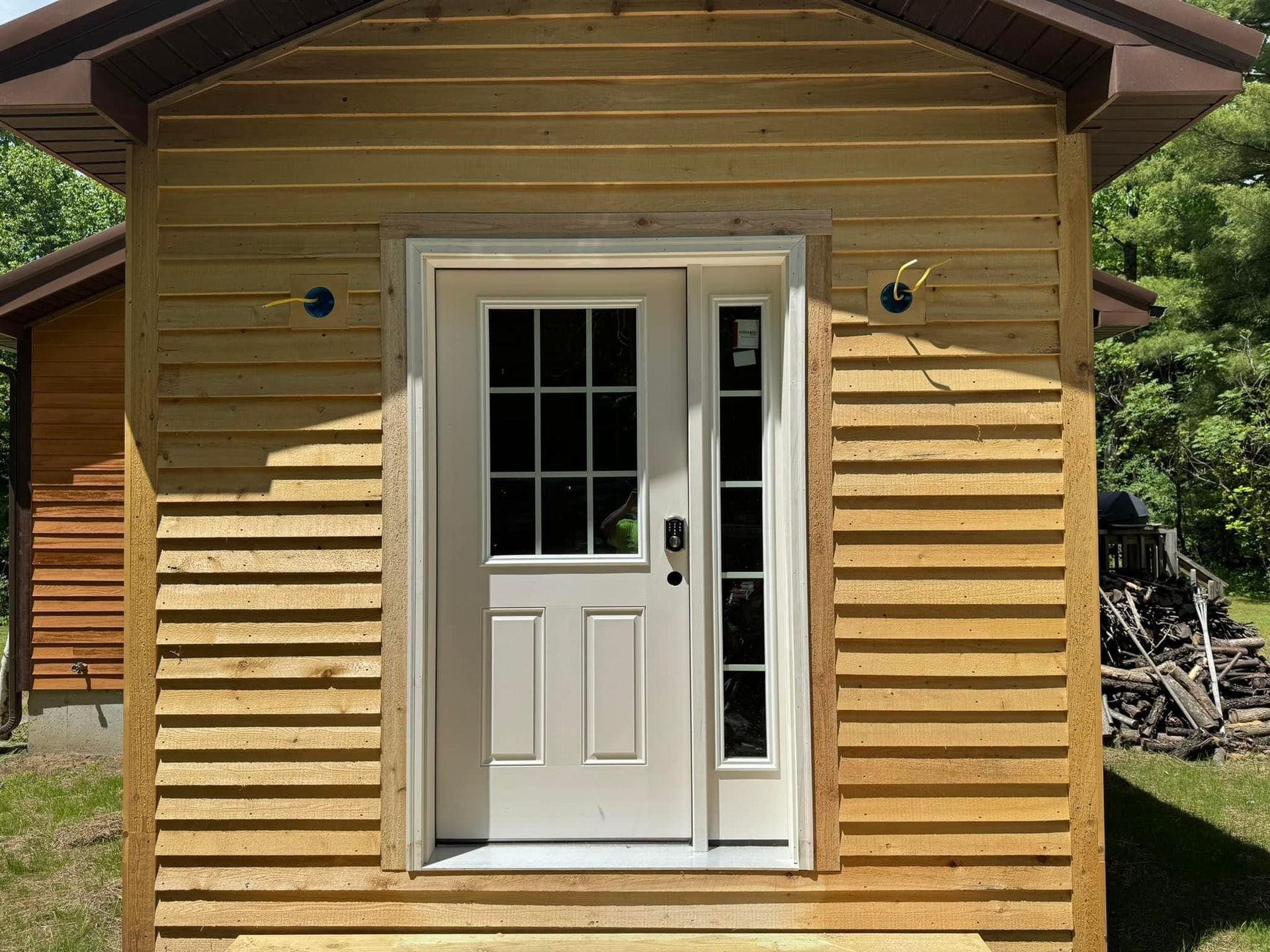 Front view of a small wooden cabin with a white door and window, lit by sunlight