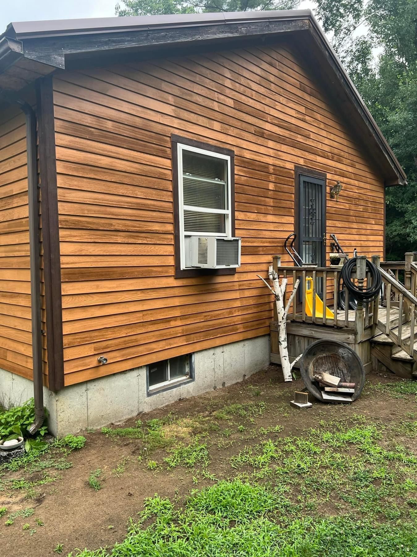 Wood-sided house exterior with a window air conditioner and small porch, seen from the side.