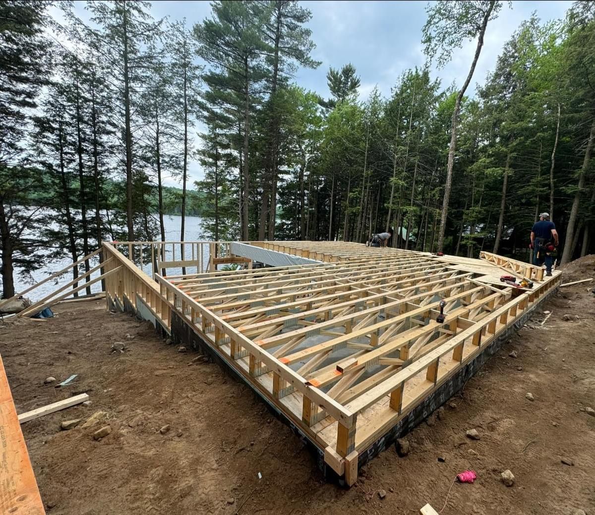 Wooden house foundation under construction in a forested lakeside area