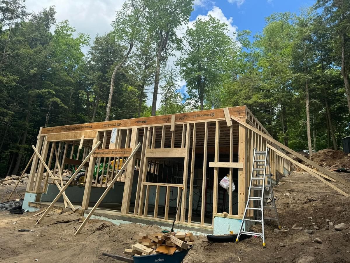 Partially built wooden house frame with ladders on a wooded construction site
