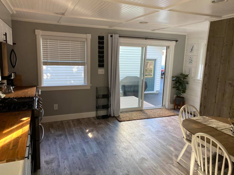 Bright kitchen and dining area with gray walls, wood floor, sliding glass door, and a small table by the window.