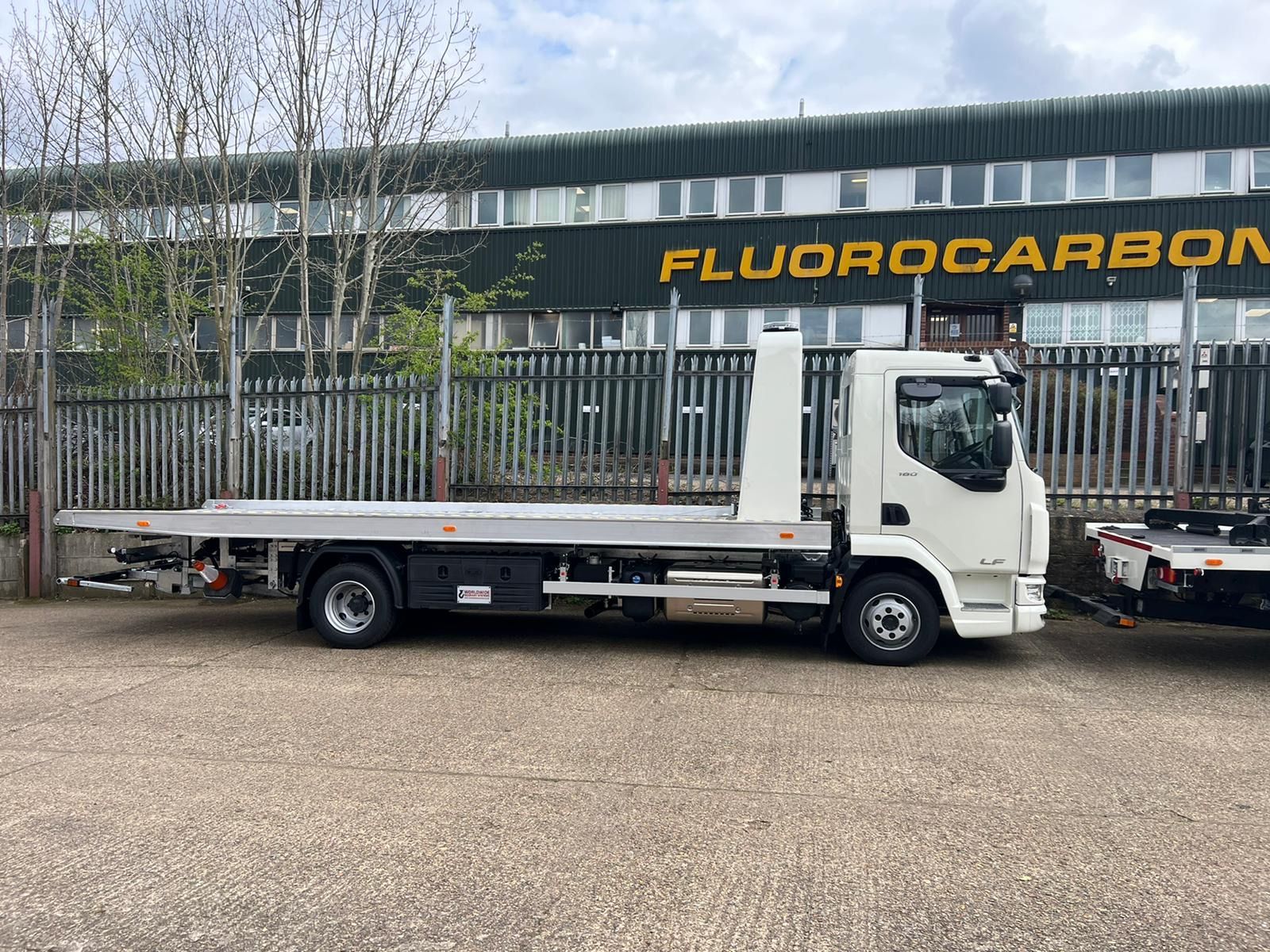 A tow truck is parked in front of a building that says fluorocarbon.