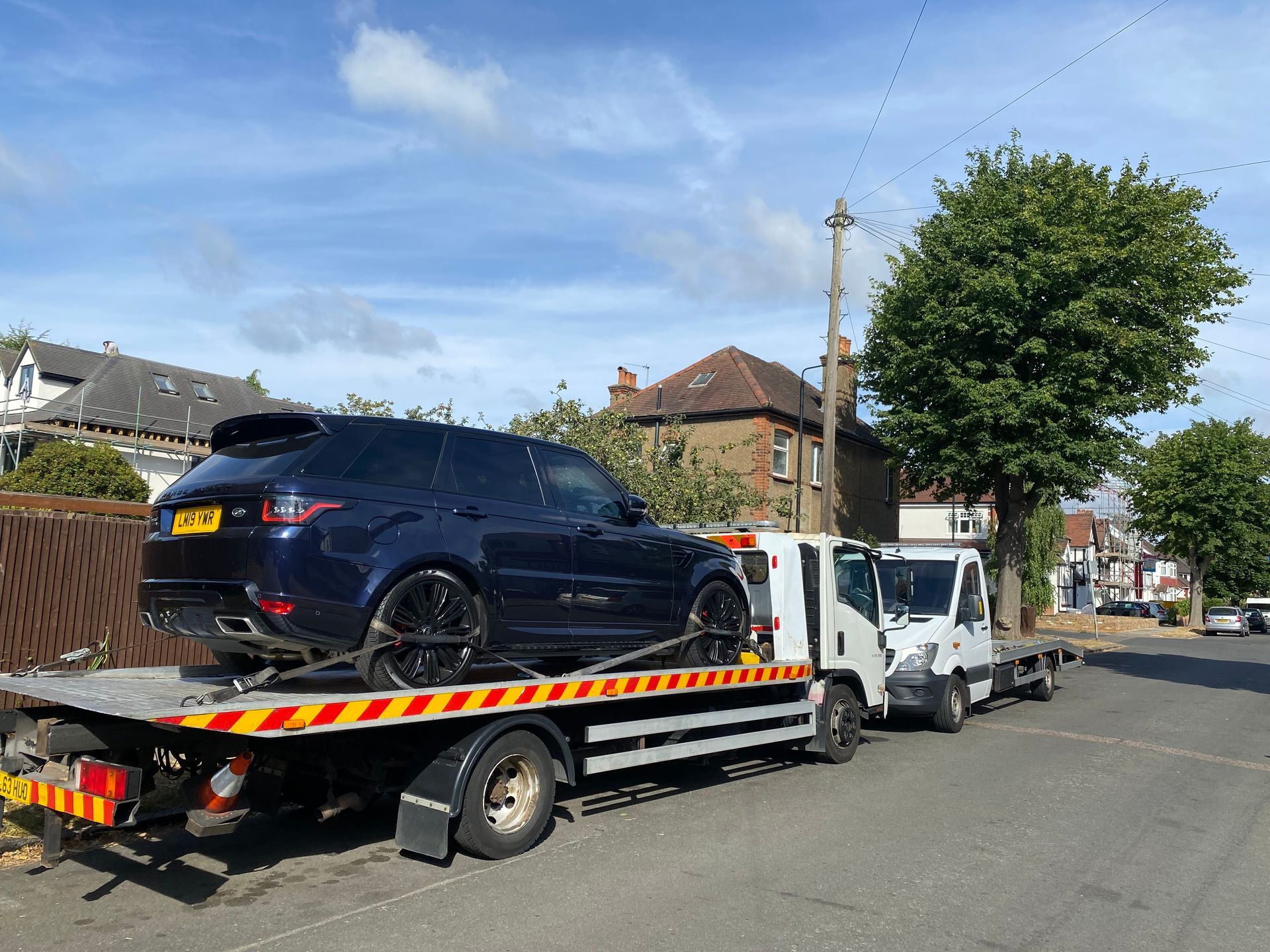 A dark blue Range Rover SUV loaded on a flatbed tow truck on a residential street.