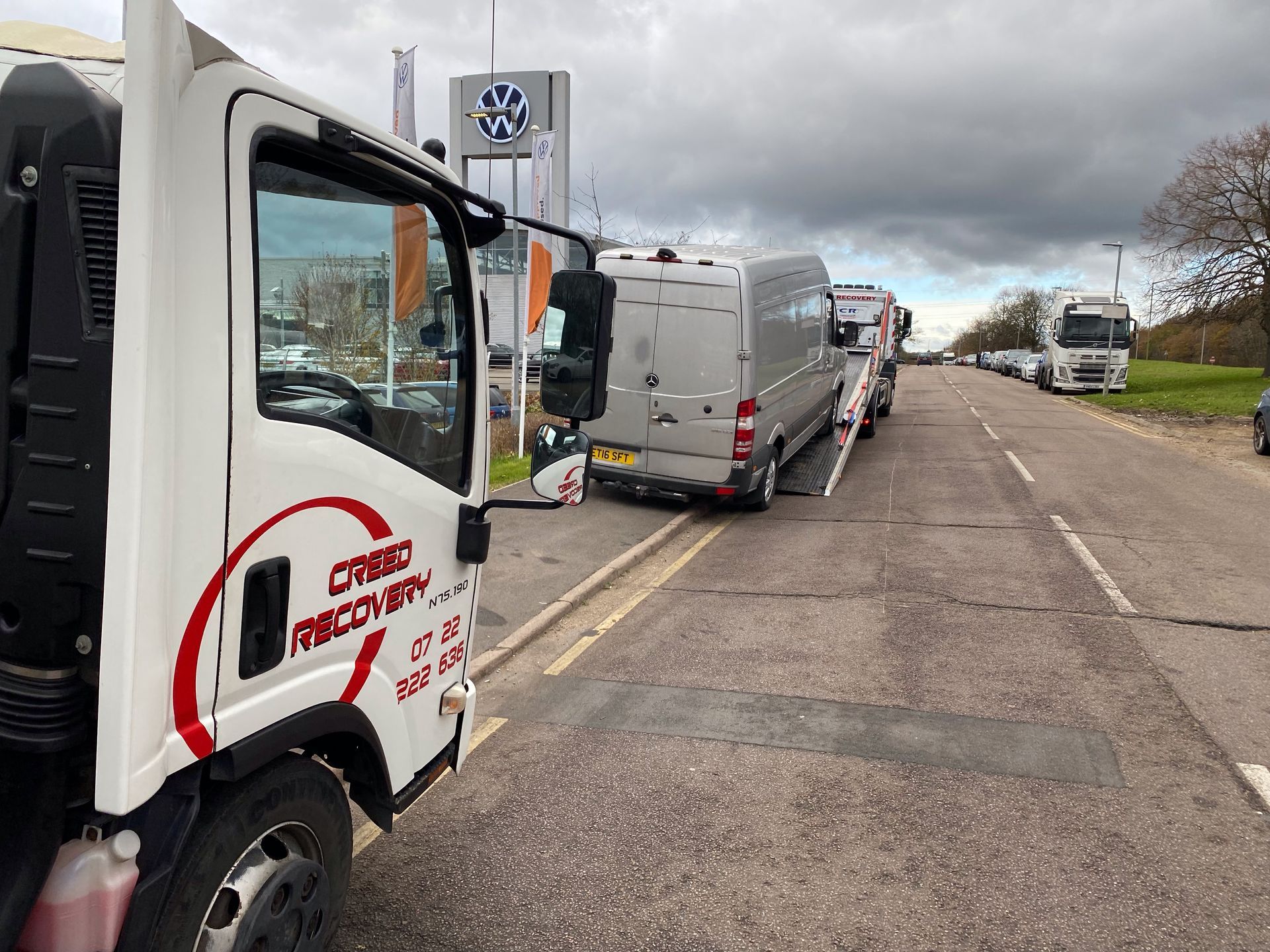 A white truck is parked on the side of the road next to a row of vans.