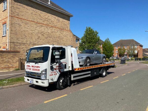 A tow truck with a car on the back is parked on the side of the road.