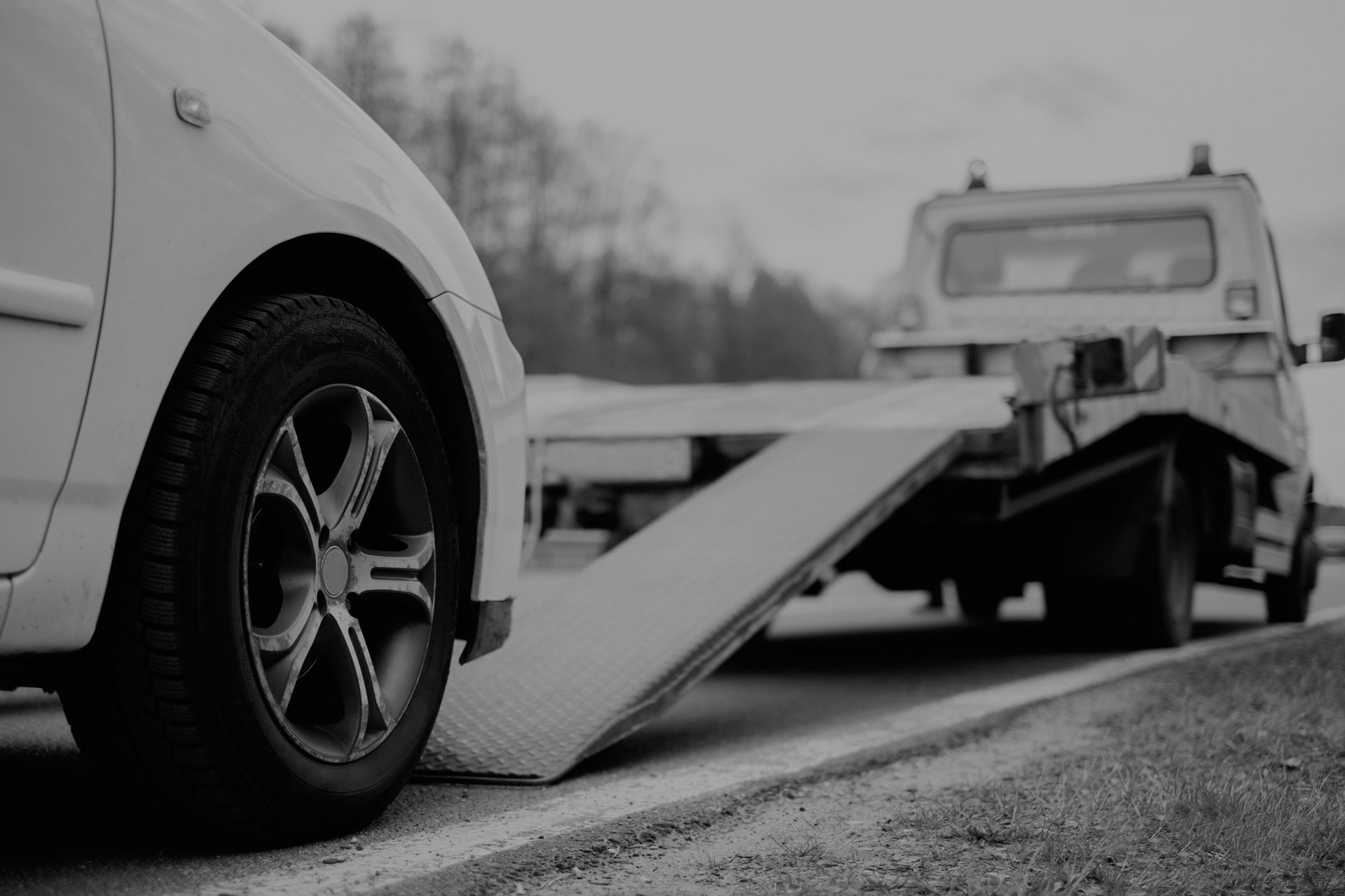 A car is being towed by a tow truck on the side of the road.
