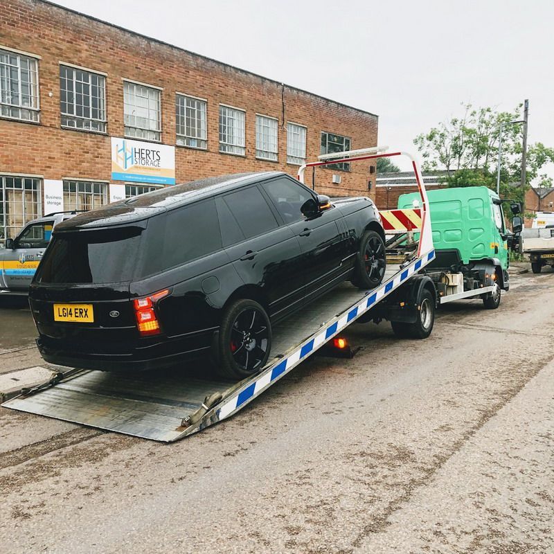 Black Range Rover being towed on a flatbed truck in front of a brick building.