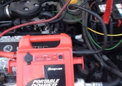 A snap-on portable power device is sitting under the hood of a car