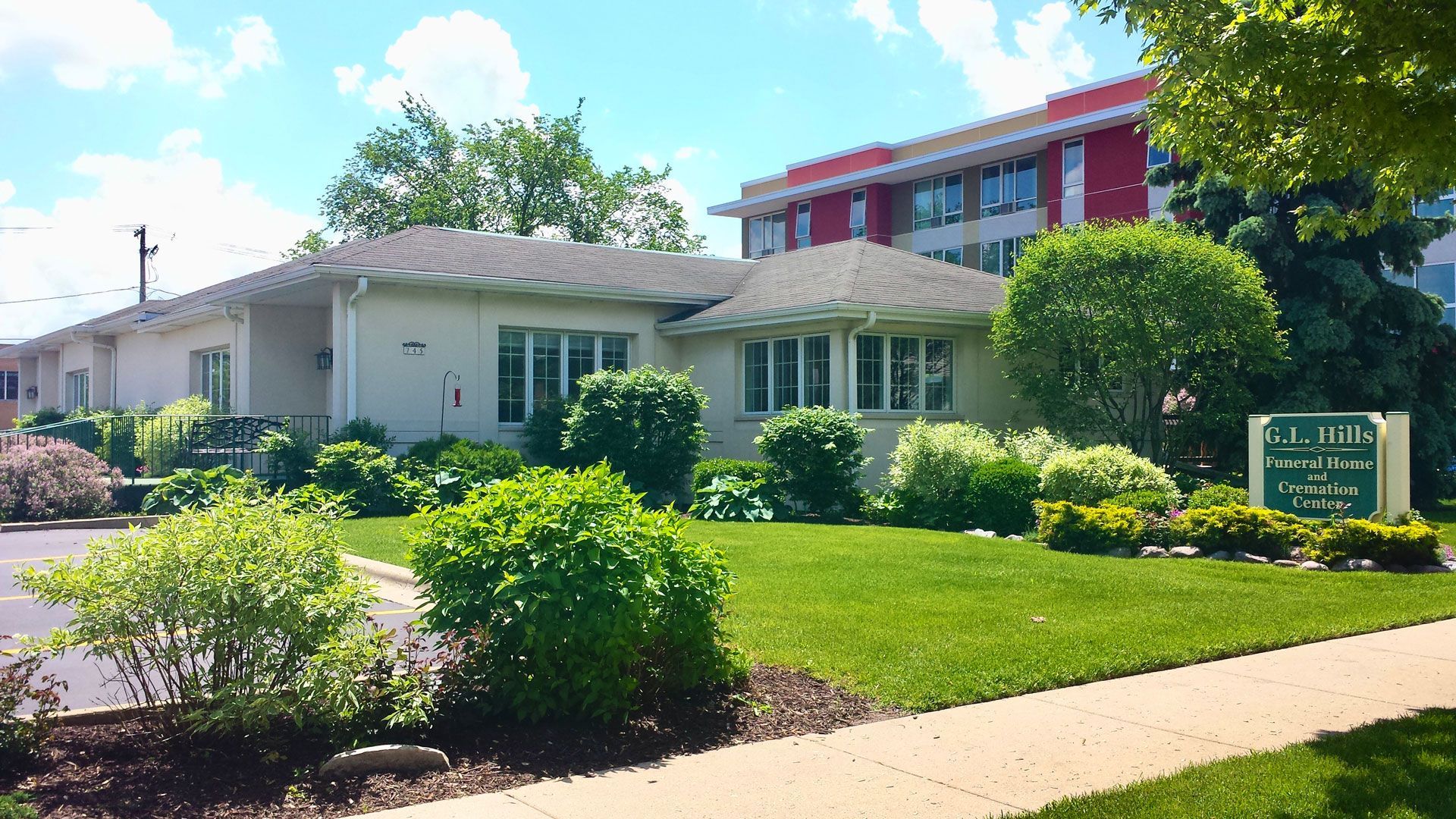 Single-story white building with green lawn, shrubs, and a sign by the sidewalk under a blue sky