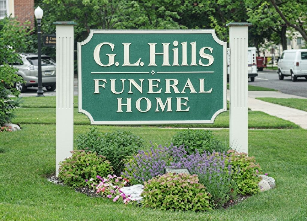 G.L. Hills Funeral Home sign in a landscaped yard with flowers and trees behind it