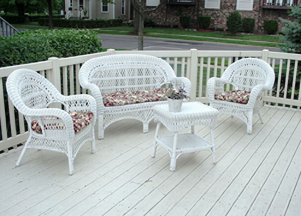 White wicker patio furniture set on a light deck with railing and potted flowers outdoors