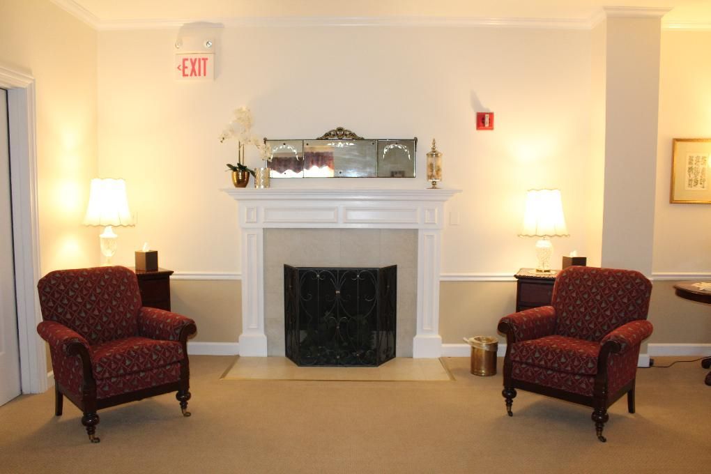 Elegant living room with white fireplace, two red armchairs, and warm lamps on either side.