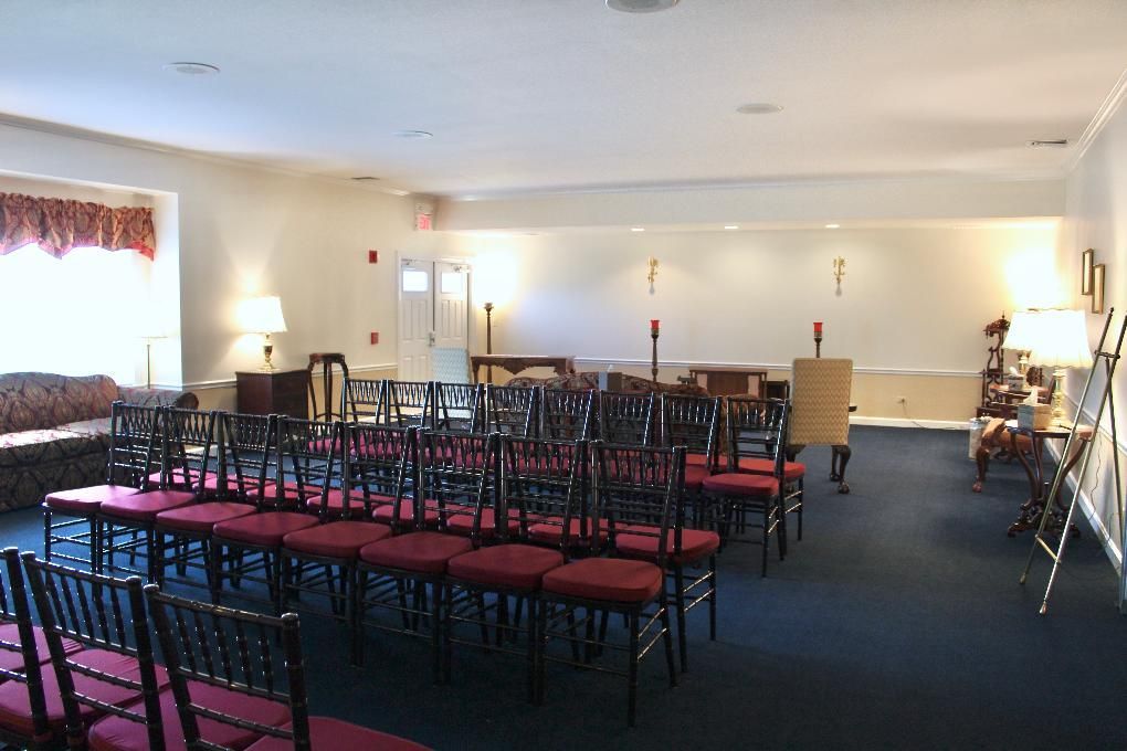 Empty banquet hall with rows of red-cushioned chairs and tables under bright ceiling lights