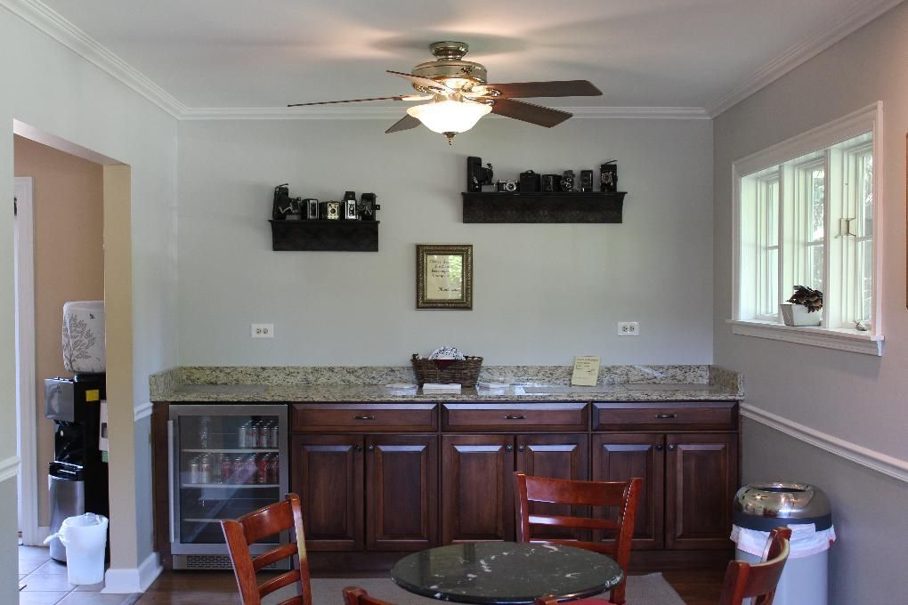 Kitchen with dark wood cabinets, granite countertop, ceiling fan, and a small table by a window.