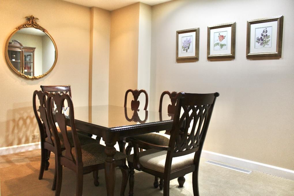 Formal dining room with dark wood table and chairs, beige walls, round mirror, and framed artwork.