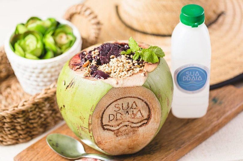 Um coco cheio de comida e uma garrafa de água em uma tábua de corte.