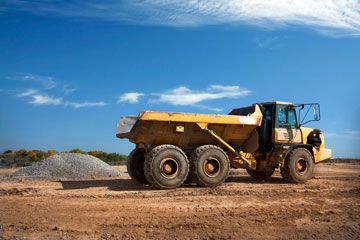 A yellow dump truck is parked in a dirt field.