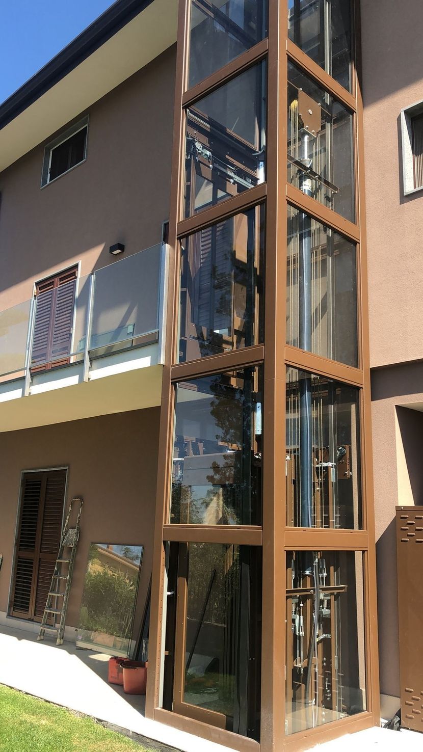 Esterno di un vano ascensore in vetro annesso a un condominio beige.
