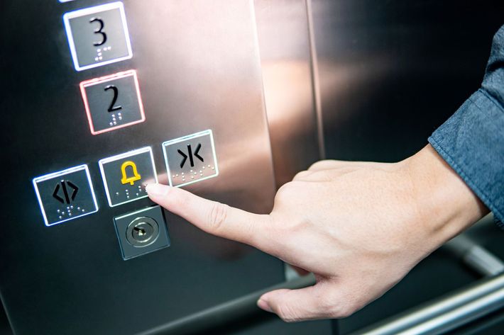 Una mano preme il pannello dei pulsanti di un ascensore, dove sono visibili i numeri del secondo e del terzo piano.