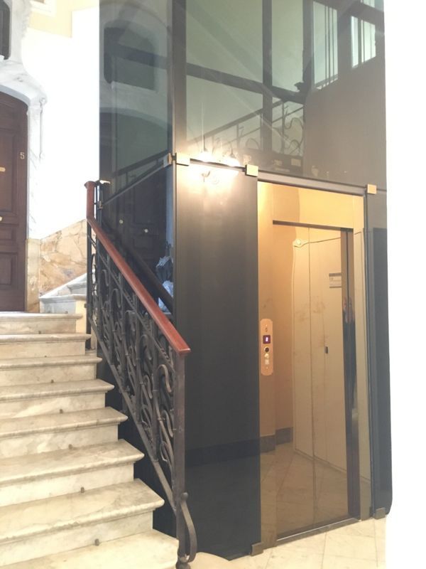 Ascensore in vetro accanto a una scala in pietra nell'atrio dell'edificio.