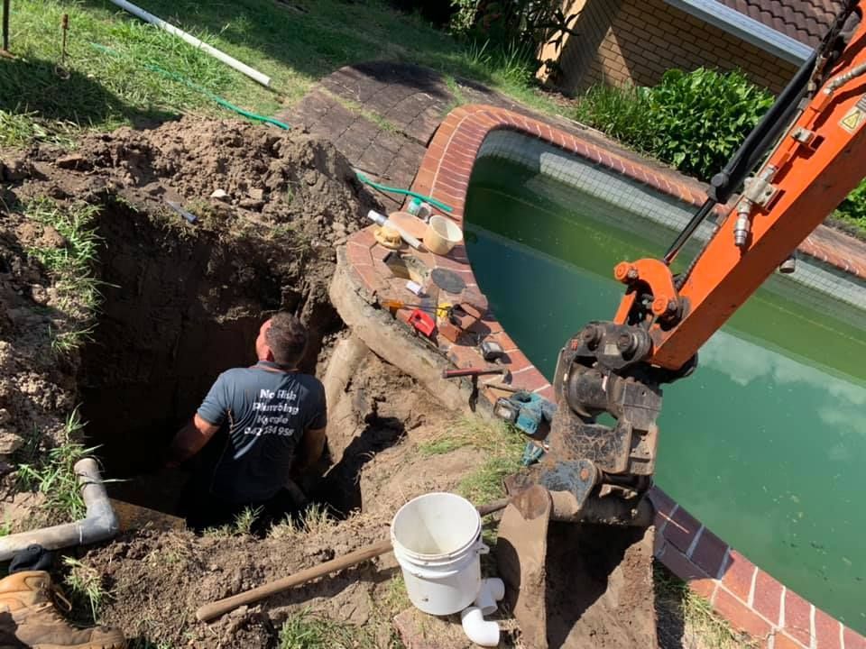 A plumber is working in a hole next to a pool — No Risk Plumbing Kyogle Pty Ltd in Geneva, NSW