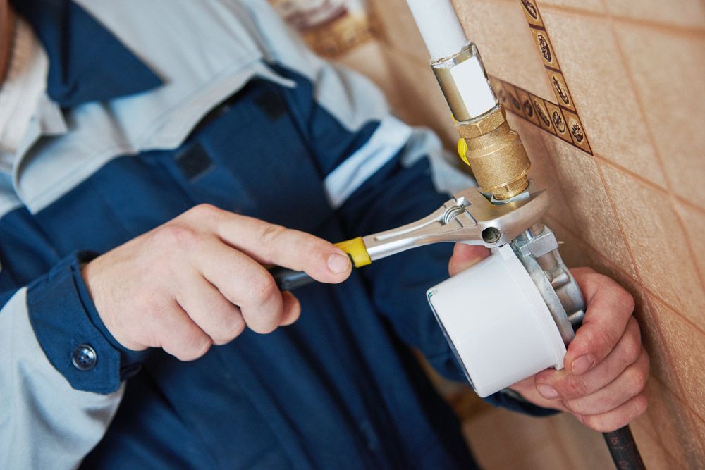 A Man Is Fixing A Pipe With A Wrench — No Risk Plumbing Kyogle Pty Ltd in Geneva, NSW