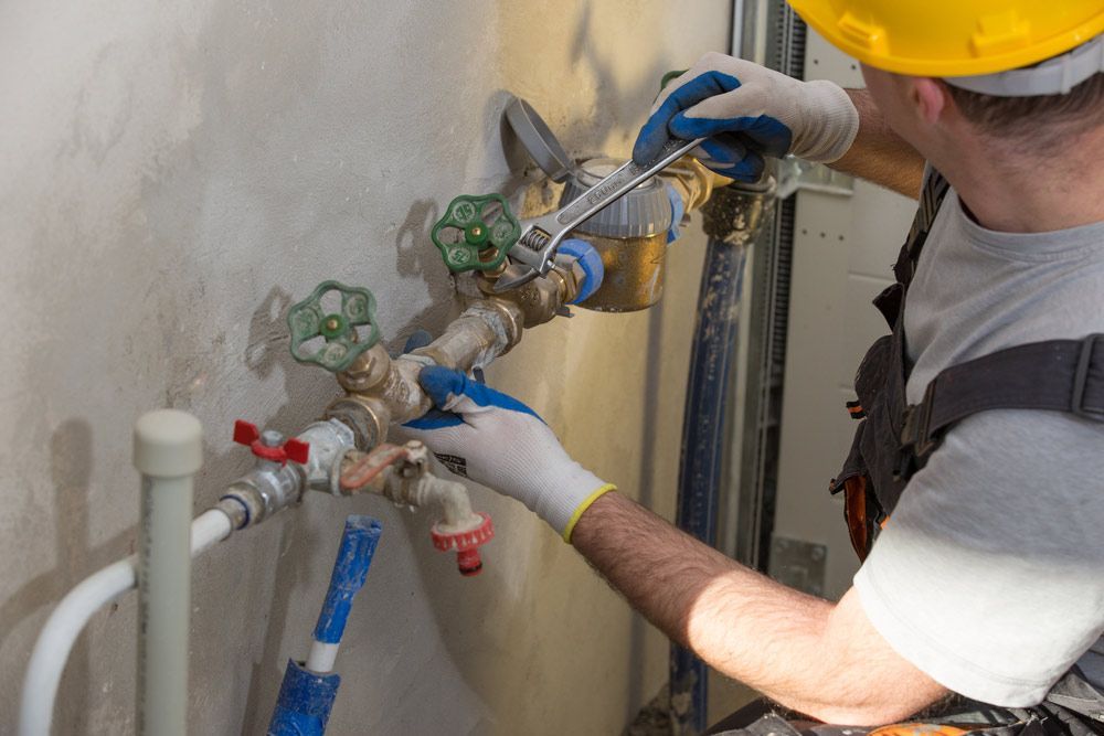 A Man Is Fixing A Water Pipe With A Wrench — No Risk Plumbing Kyogle Pty Ltd in Geneva, NSW