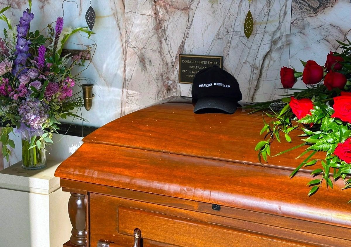 Wooden casket with flowers and a hat on top.