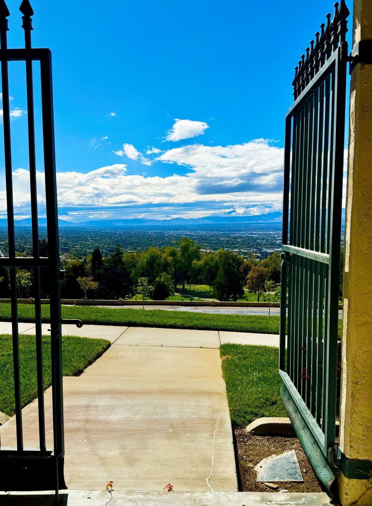 Open black gate revealing a city view under a blue sky with clouds.