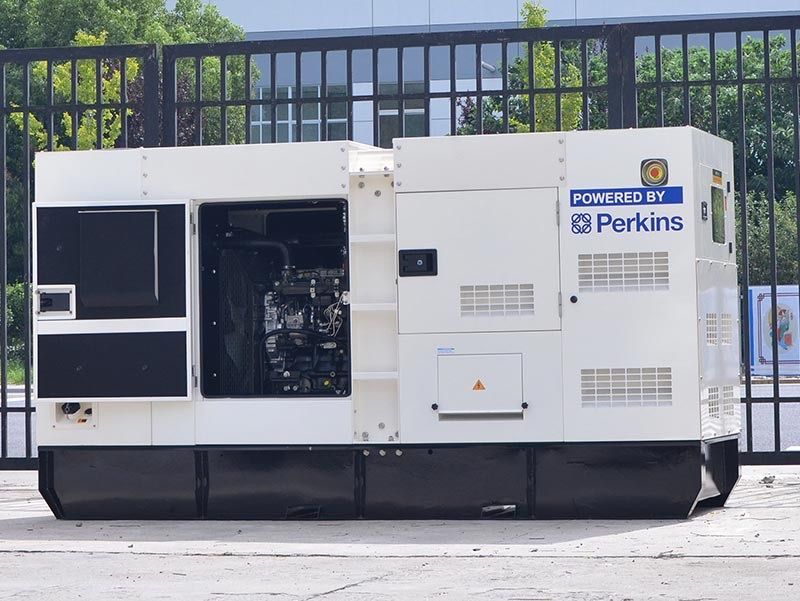 Générateur industriel blanc avec le logo « Powered by Perkins » devant une clôture métallique.
