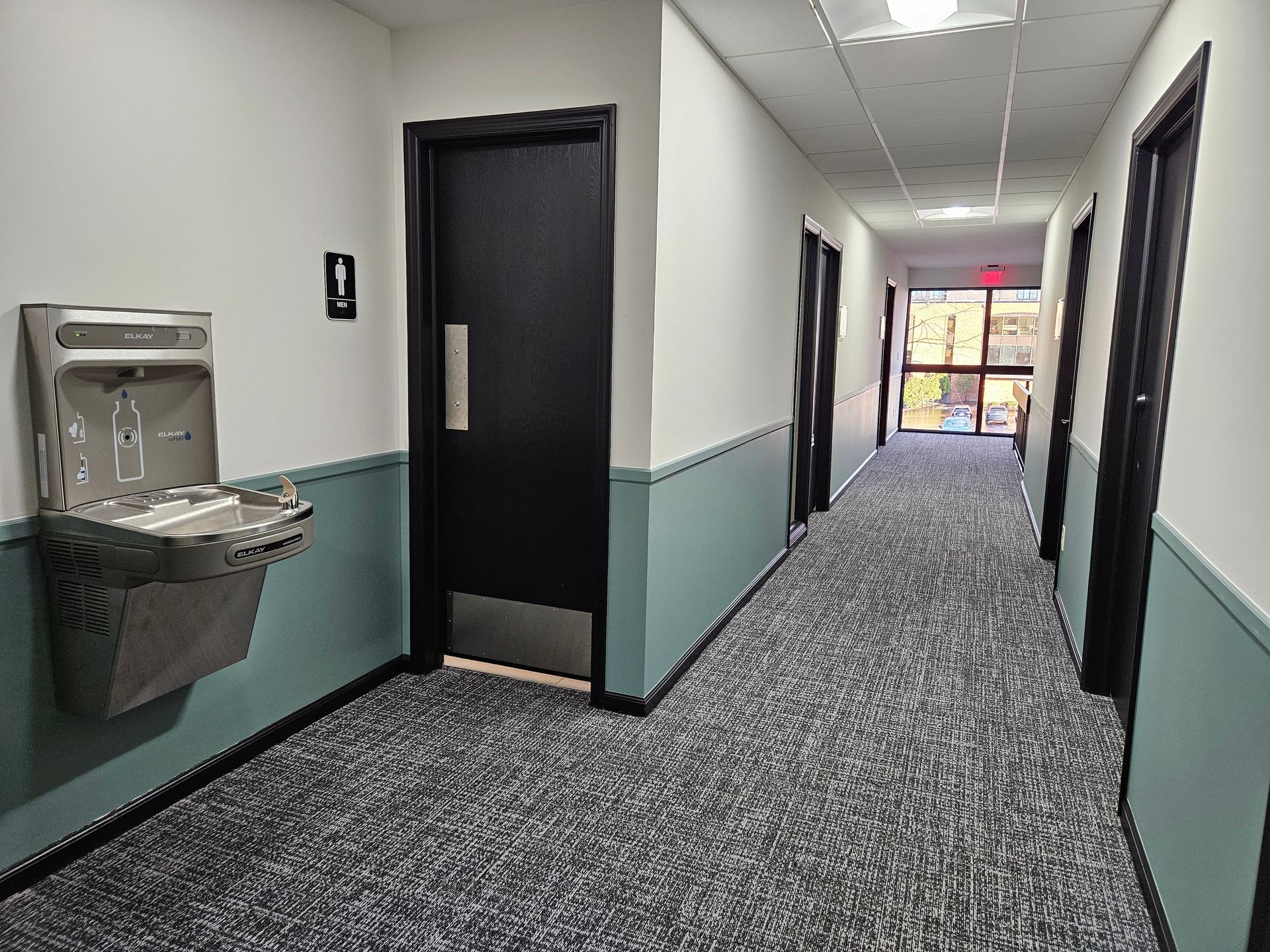 A long hallway with a water fountain and a door.