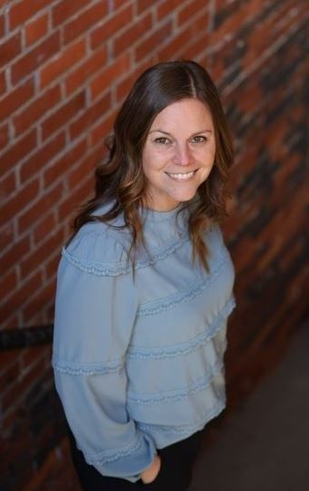 A woman in a blue sweater is standing in front of a brick wall.