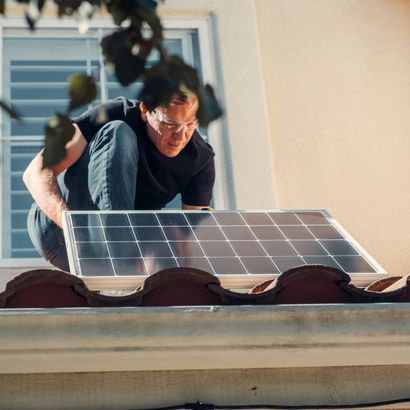 A man is installing a solar panel on the roof of a building