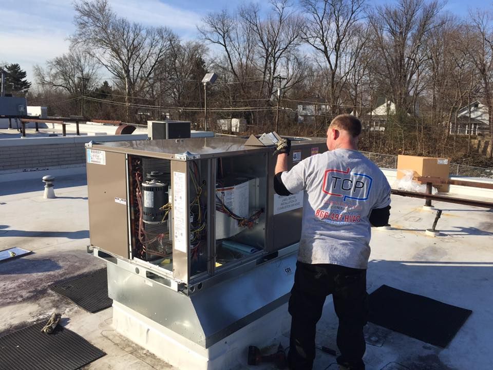 A man is working on an air conditioner on the roof of a building.