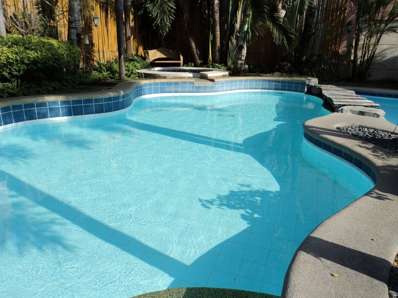 Swimming pool with ladder, colorful inflatable ring and beach ball floating in clear blue water.