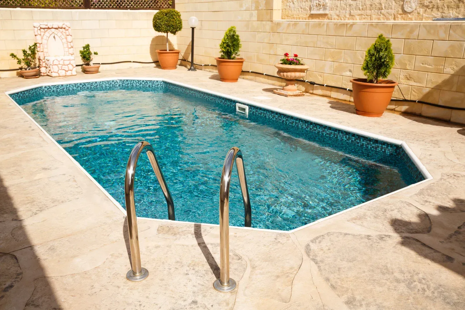Person tests pool water with a handheld meter. Blue tiled pool and cleaning equipment visible.