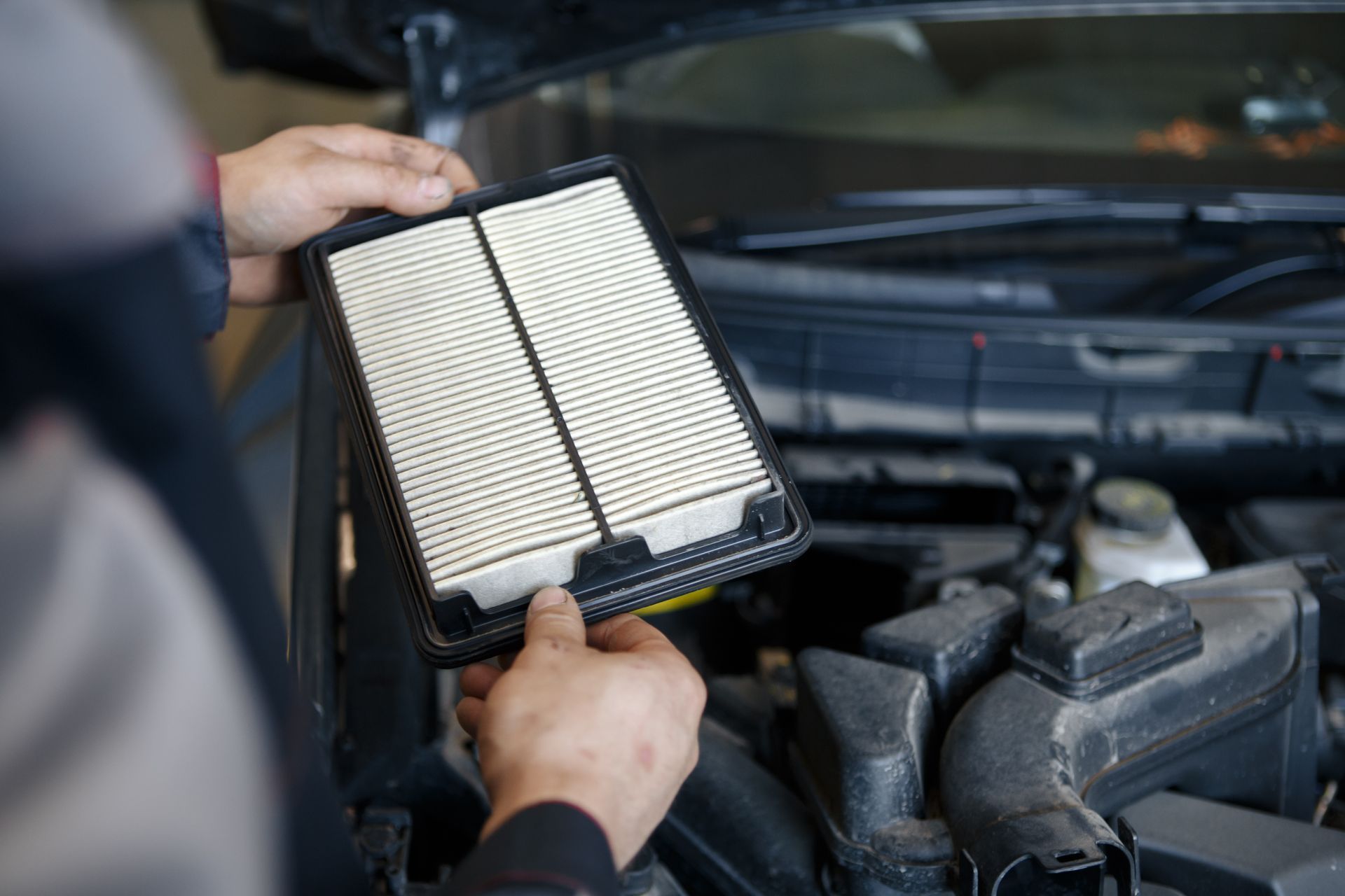 A mechanic holding a clean engine air filter over a car engine bay A mechanic holding a clean engine air filter over a car engine bay