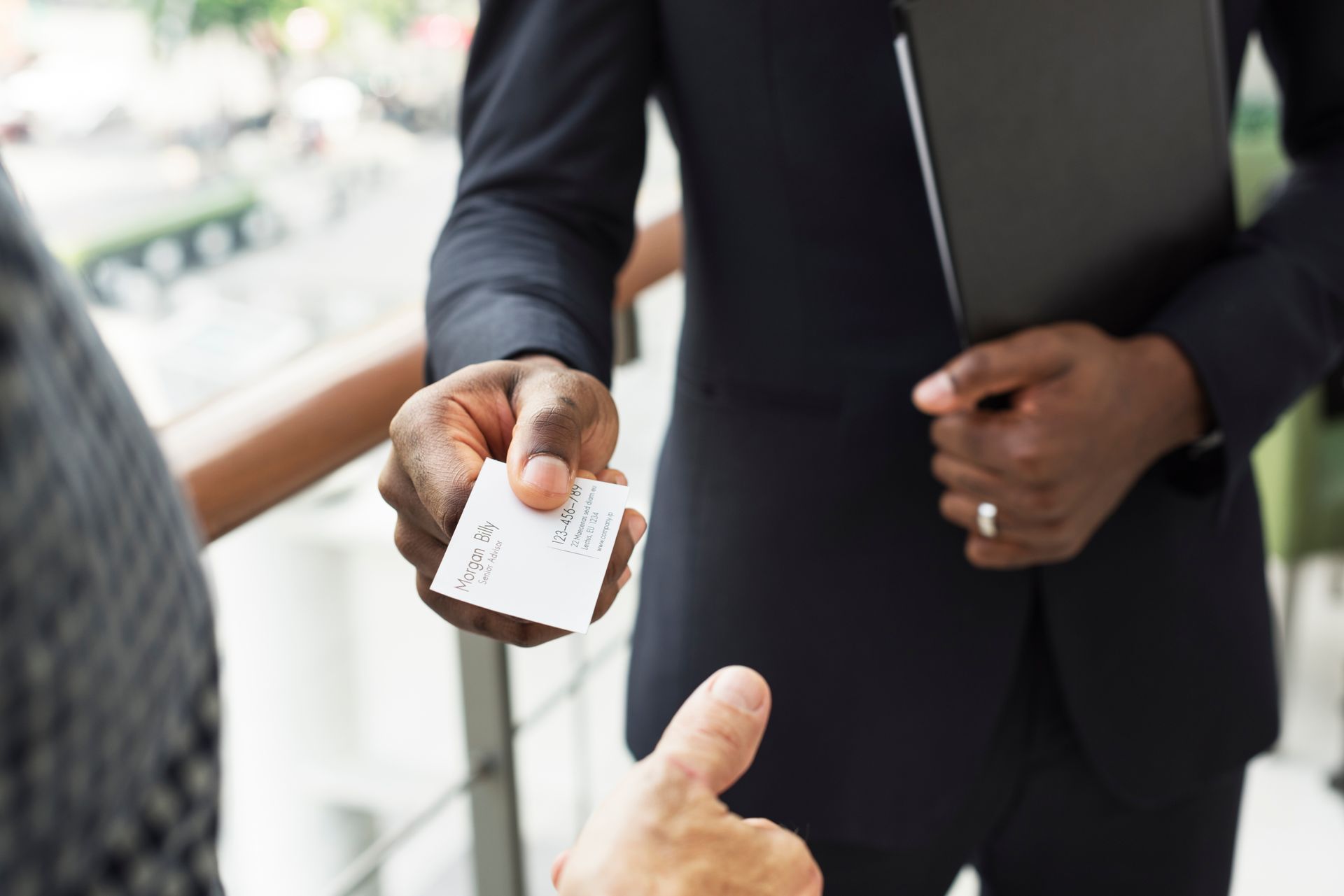 Close-up of an individual handing a business card to another person.